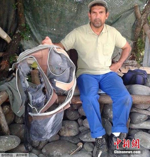 圖為當(dāng)?shù)貢r間7月30日，留尼旺島上的一名海岸清潔人員展示他找到的一個手提箱的殘骸。